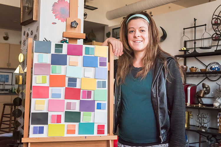 Megan Czerwinski posing with a canvas decorated in bright color swatches.