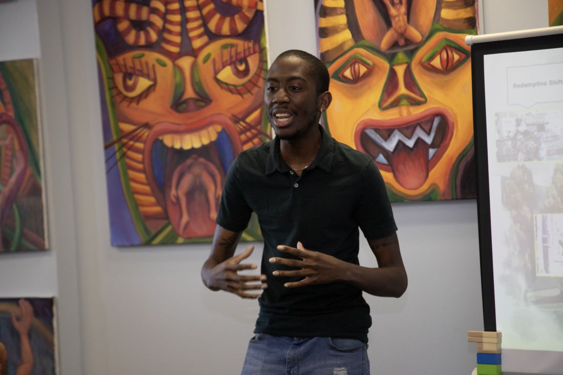 Speaker presenting in front of hanging artwork.