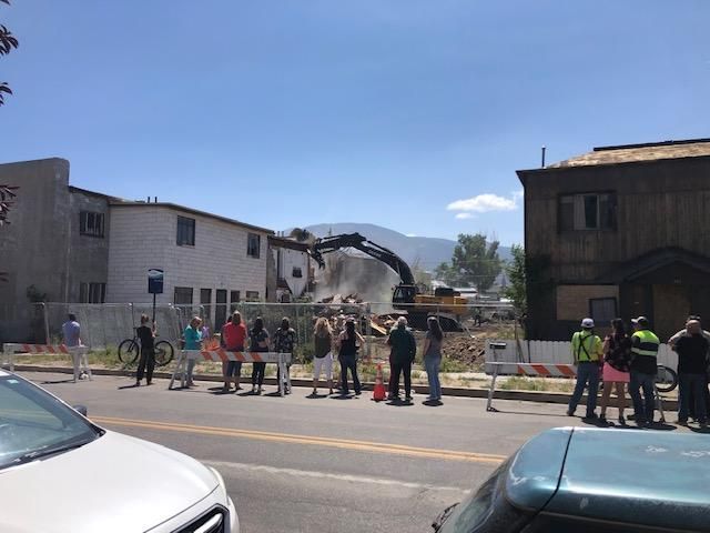 A group of people watch heavy machinery demolish the buildings on site