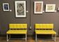 Photograph of two yellow chairs in a gallery with four photos on the wall