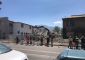 A group of people watch heavy machinery demolish the buildings on site