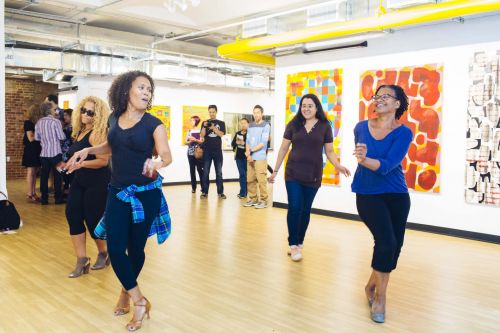 Dancers in a beautiful, bright indoor space with artworks on the wall behind them.