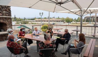 A group of 8 people sit outside at a patio table. 