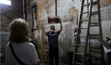 An image of Lucas holding a photo of the feed in grain while he leads of tour of people inside the brick building