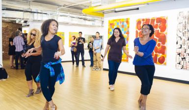 Dancers in a beautiful, bright indoor space with artworks on the wall behind them.